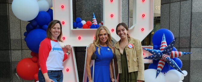 Jacki Mowery, Sheila Hess, and Riley Flanagan standing in front of large white LOVE letters at corporate event.
